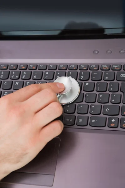 Hand examining laptop keyboard with stethoscope — Stock Photo, Image