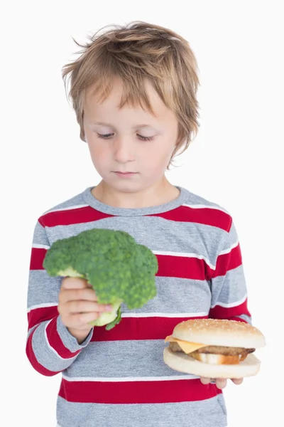 Jeune garçon tenant brocoli et hamburger — Photo