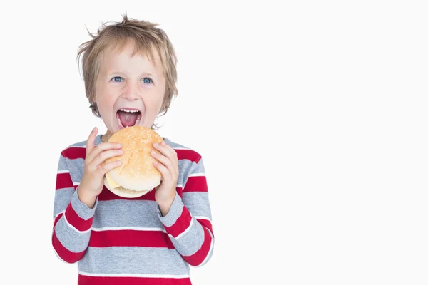 Eszik hamburgert, vidám fiatal fiú — Stock Fotó