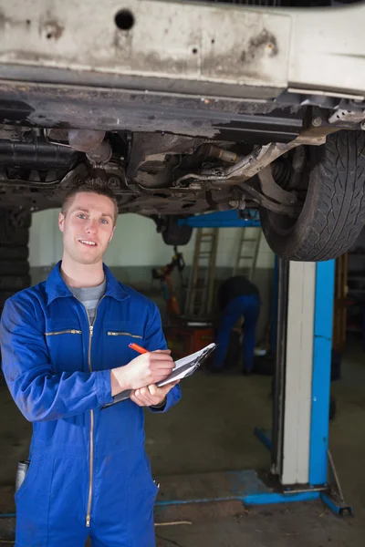 Repairman preparing checklist under car — Stock Photo, Image