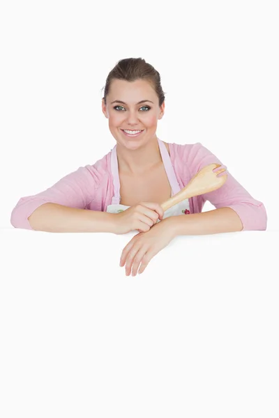 Maid holding spoon as she leans on blank billboard — Stock Photo, Image