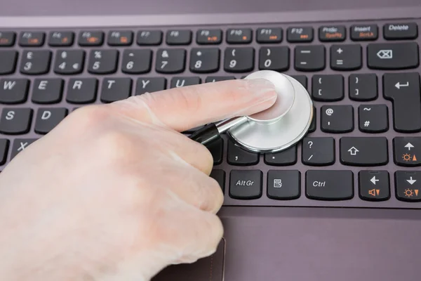 Mão examinando teclado portátil com estetoscópio — Fotografia de Stock