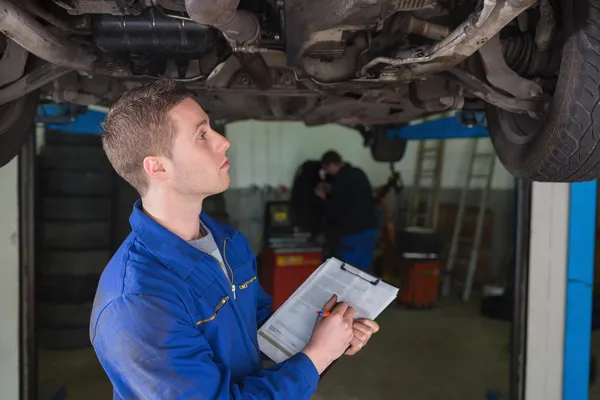 Mecánico bajo el coche preparando la lista de verificación — Foto de Stock