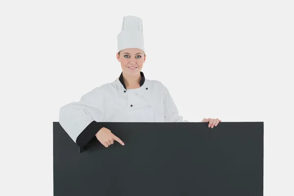 Happy female chef pointing at black billboard — Stock Photo, Image