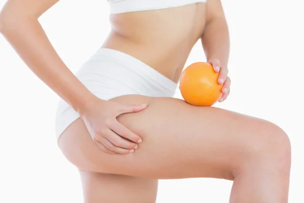 Femme serre la peau de cellulite sur la cuisse comme elle tient orange — Photo