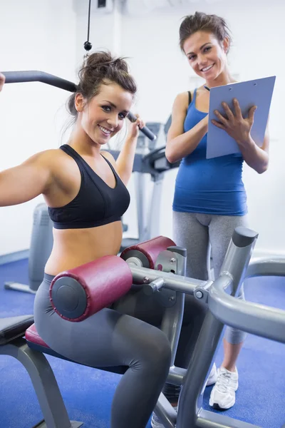 Glad kvinnliga tränare och klienten på vikter maskin — Stockfoto
