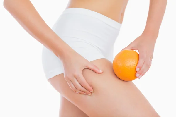 Frau drückt Fett auf den Oberschenkel, während sie orange hält — Stockfoto