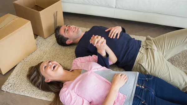 Laughing couple lying on floor with moving boxes — Stock Photo, Image