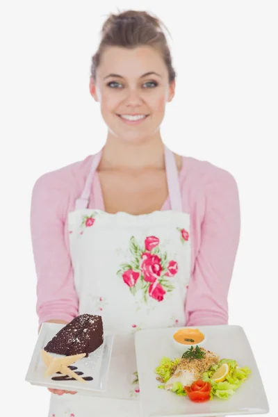 Woman in apron holding plates of pastry and healthy meal — Stock Photo, Image