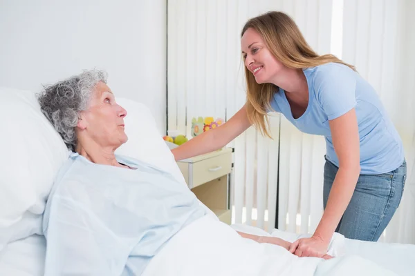 Mulher sorridente segurando a mão de um paciente em um quarto — Fotografia de Stock