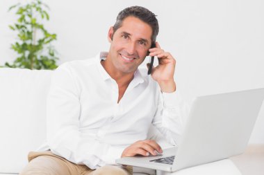 Smiling man using his laptop and phoning clipart