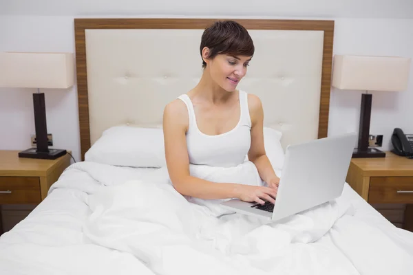 Γυναίκα που χρησιμοποιεί φορητό υπολογιστή στο κρεβάτι — Φωτογραφία Αρχείου