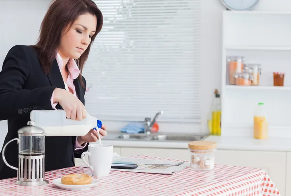 Business woman pouring milk in coffee cup — Stock Photo, Image