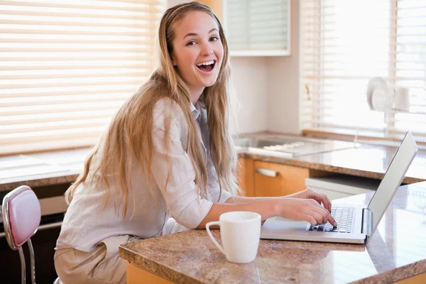 Wesoły młoda kobieta korzysta z laptopa w kuchni — Zdjęcie stockowe