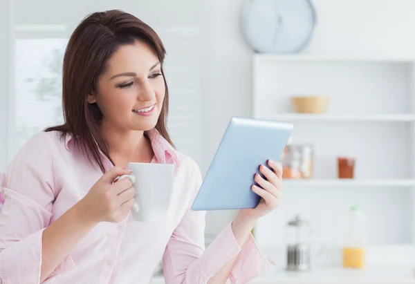 Usmívající se žena s šálek kávy při pohledu na digitální tabletu — Stock fotografie