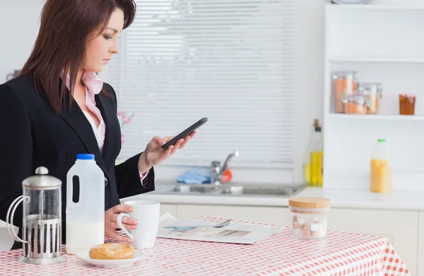 Business woman text messaging while having breakfast in kitchen — Stock Photo, Image