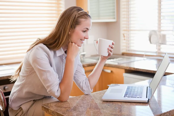 Счастливая женщина с чашкой кофе смотрит на ноутбук — стоковое фото