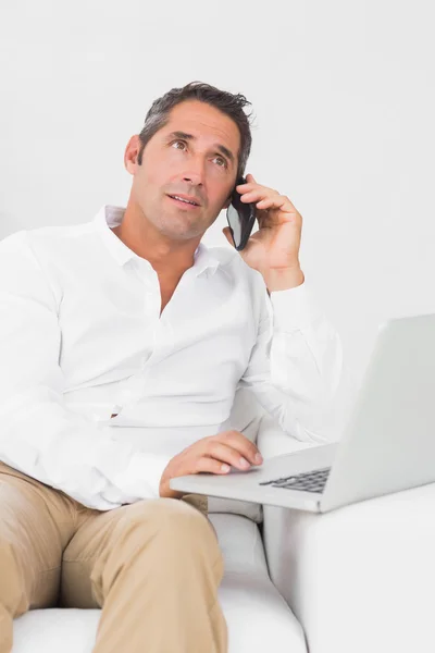 Uomo che utilizza il suo computer portatile mentre telefona — Foto Stock