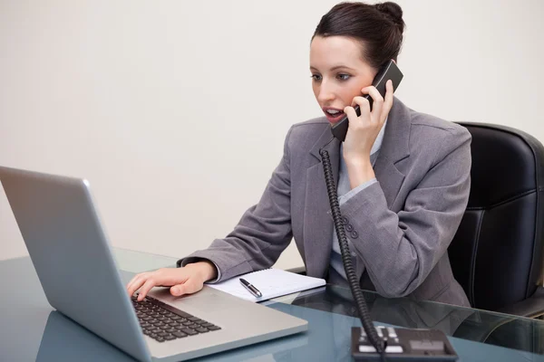 Geschokt zakenvrouw met behulp van laptop terwijl op oproep — Stockfoto