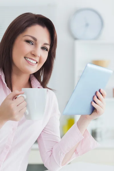 Улыбающаяся женщина с чашкой кофе и цифровым планшетом — стоковое фото