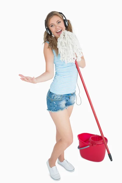 Woman holding broom as microphone and listening music over headp — Stock Photo, Image