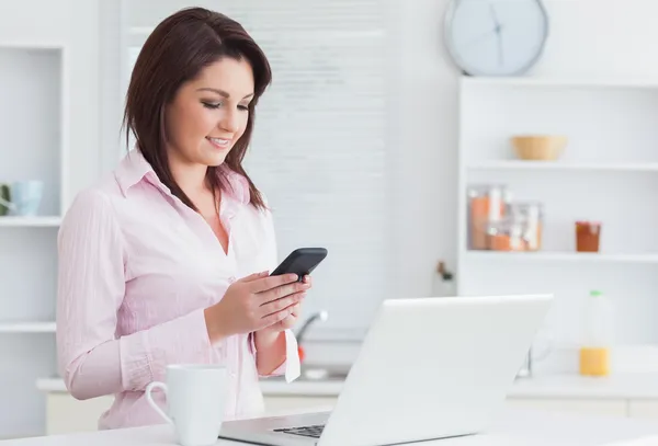 Kvinna med kaffekoppen och laptop med hjälp av mobiltelefon — Stockfoto