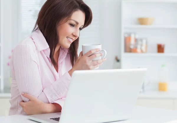 Улыбающаяся женщина с чашкой кофе с помощью ноутбука — стоковое фото