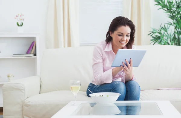 Mulher com vinho e tigela usando tablet digital no sofá — Fotografia de Stock
