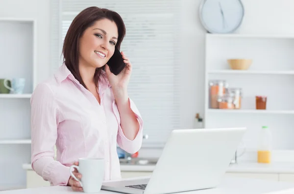 Femme avec tasse de café et ordinateur portable en utilisant un téléphone portable — Photo