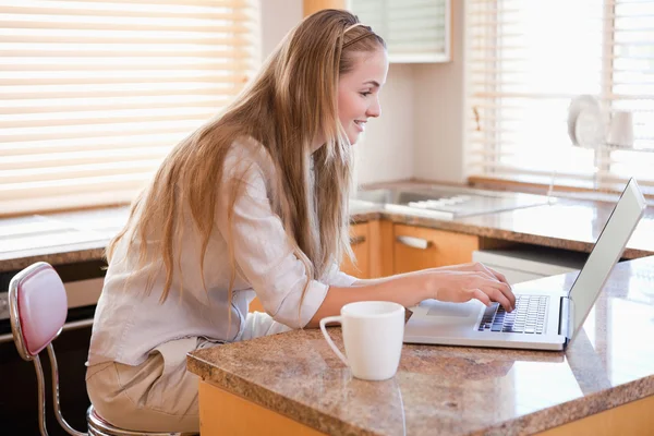 Jovem mulher usando laptop na cozinha — Fotografia de Stock