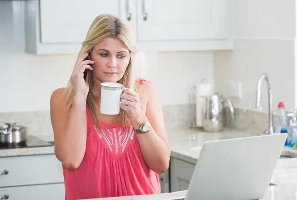 Vrouw met laptop en koffie cup op oproep in keuken — Stockfoto