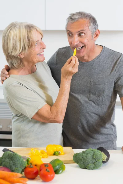 Marido sorrindo degustando uma fatia de pimenta amarela — Fotografia de Stock