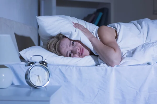 Mujer cubriendo orejas con almohada como anillos de despertador — Foto de Stock