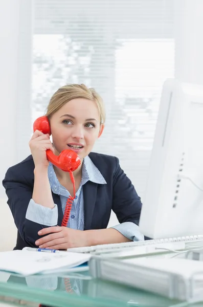 Ejecutiva usando teléfono fijo rojo en el escritorio — Foto de Stock