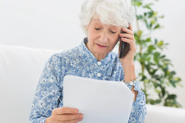 Ältere Frau liest Zeitung am Telefon — Stockfoto