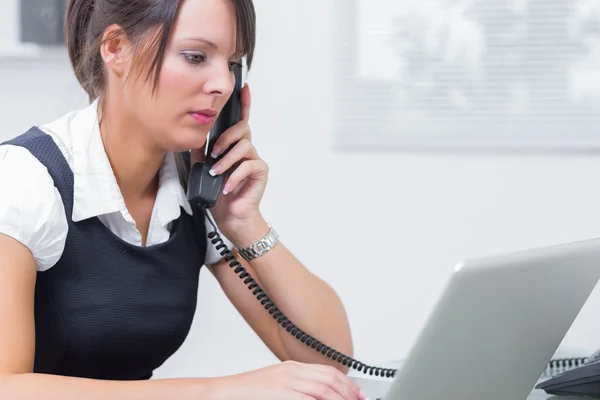 Executive using laptop and landline phone at office — Stock Photo, Image