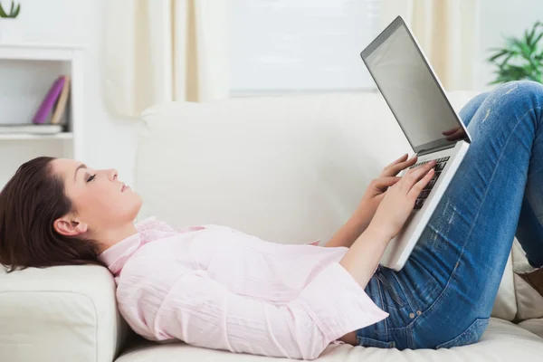 Mulher casual deitada no sofá e usando laptop Imagem De Stock