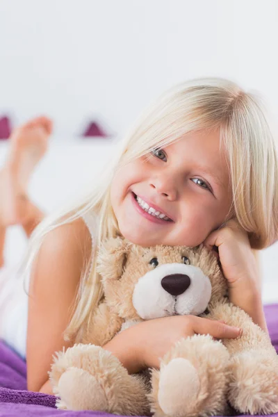 Lächelndes Mädchen mit ihrem Teddybär auf einem Bett liegend lizenzfreie Stockbilder