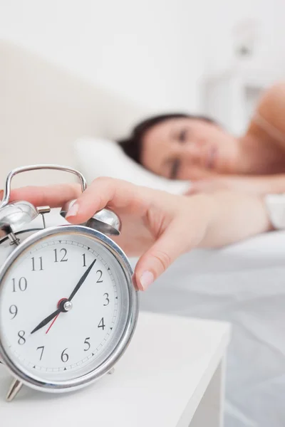 Woman in bed extending hand to alarm clock Royalty Free Stock Images