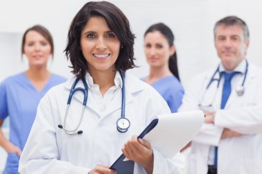 Female doctor with clipboard and her team smiling clipart