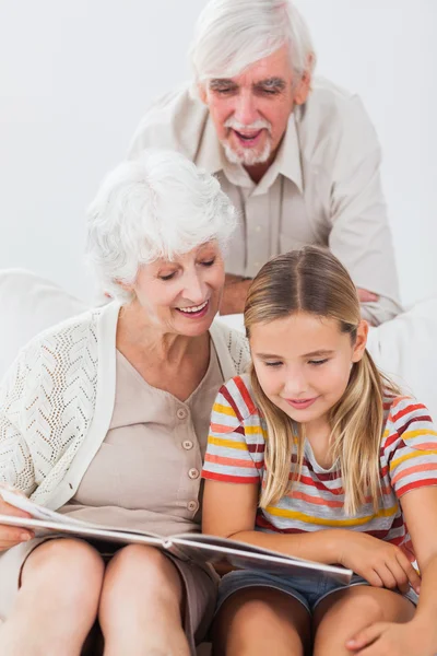 Улыбающаяся девушка читает с бабушкой и дедушкой — стоковое фото