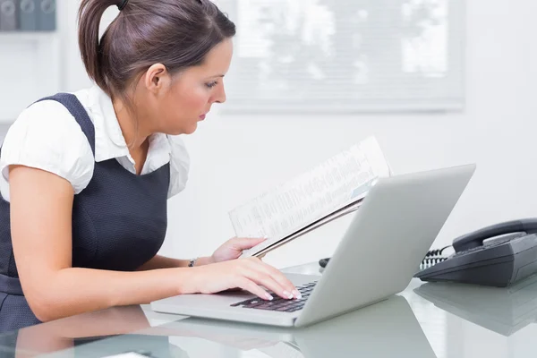 Iş kadını ofiste dizüstü bilgisayar kullanırken kağıt okuma — Stok fotoğraf