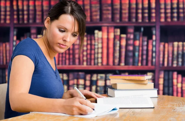 Linda chica escribiendo en el cuaderno en la biblioteca — Foto de Stock