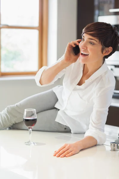 Woman phoning in kitchen with a glass of wine — Stock Photo, Image