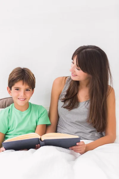 Lachende moeder en zoon lezen in bed — Stockfoto