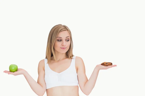 Молодая женщина с яблоком смотрит на печенье — стоковое фото
