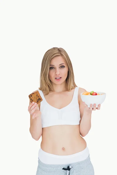 Portrait of young woman holding cookie and fruit bowl — Stock Photo, Image