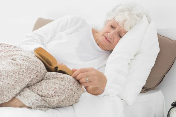 Alte Frau liegt auf dem Bett und liest — Stockfoto