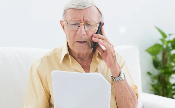 Idoso lendo papéis ao telefone — Fotografia de Stock