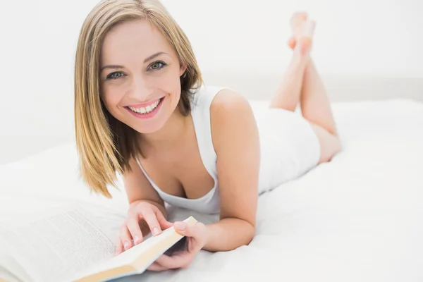 Portrait of young woman reading book in bed — Stock Photo, Image